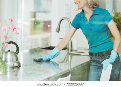 Professional House Cleaning Service Concept, Smiling Woman Wiping Down Marble Kitchen Countertop Using Domestic Cleaner, Cloth And Rubber Household Gloves