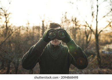 Professional hunter looking through binoculars. Man on the hunt in the middle of forest. 