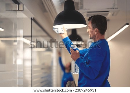 Professional hygiene maintenance. A cleaner cleans the chandelier in the office while in the background another cleaner washes the glass panels Foto d'archivio © 