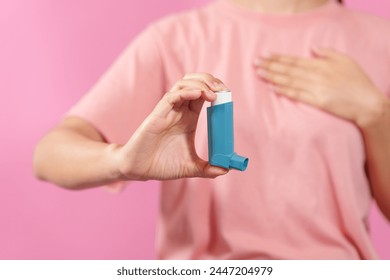 A professional image featuring a female hand holding an asthma inhaler with fingers against a soft pink isolated background, highlighting respiratory health and wellness. - Powered by Shutterstock