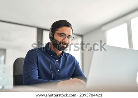 Professional Indian busy call center agent hotline representative wearing headset working on customer support service having conversation with client using laptop computer working online in office.