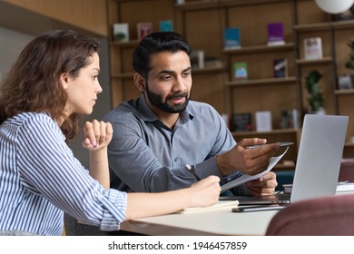 Professional indian teacher, executive or mentor helping latin student, new employee, teaching intern, explaining online job using laptop computer, talking, having teamwork discussion in office.