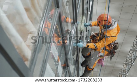professional industrial climber in helmet and rubber gloves washes windows on a tall building top view
