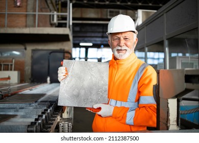 Professional industrial worker working in ceramic tile factory standing by machine and showing the product.