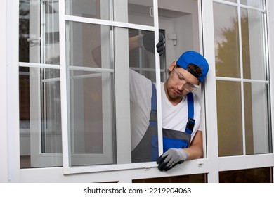 Professional installation of mosquito nets on a plastic window using external plastic or metal fasteners. Worker carefully installs the insect repellent grid on open window