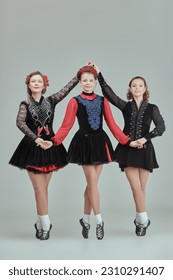 Professional Irish dance ensemble of three women in concert costumes and Ghillies Soft Shoes pose together in a row. Full-length studio portrait on a grey background. - Shutterstock ID 2310291407
