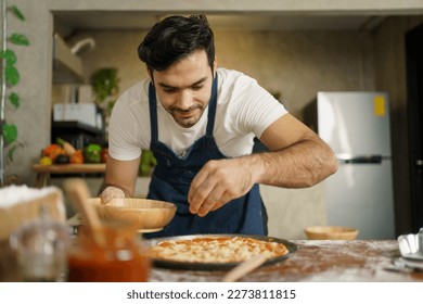 Professional Italian chef baking a cheesy Hawaiian pizza at home. Italian chef topping a Hawaiian pizza with mozzarella cheese, tomato sauce, vegetable, and meat before bake in the oven. - Powered by Shutterstock