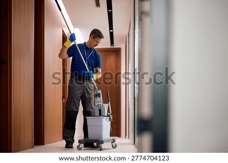 Professional janitor using mop while cleaning floors in office hallway. Copy space. 