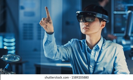 Professional Japanese Development Engineer Is Working In A AR Headset, Moving Virtual Pieces Around And Looking At Graphics In The High Tech Research Laboratory With Modern Computer Equipment.