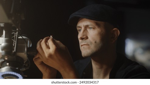 Professional jeweler in a dark workshop works on a gold ring with a diamond under a magnifying glass - Powered by Shutterstock