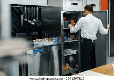 professional kitchen chef looks into fridge and chooses ingredients for cooking food concept