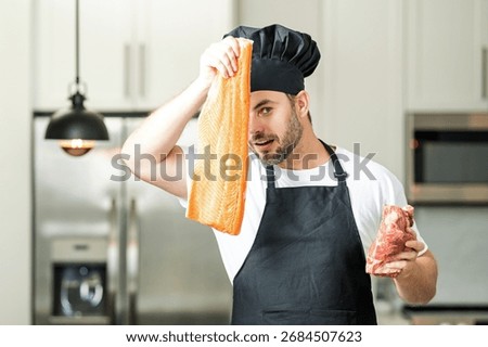 Professional kitchen. Chef with raw meat beef and fish salmon fillet. Man in uniform on kitchen. Handsome male chef in uniform with chefhat cooking raw meat beef and fish salmon fillet in the kitchen.