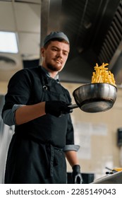 professional kitchen in the hotel restaurant chef tosses delicious french fries in a bowl