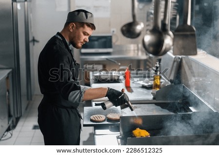 professional kitchen in hotel restaurant chef with kitchen torch browning cheese burger patty