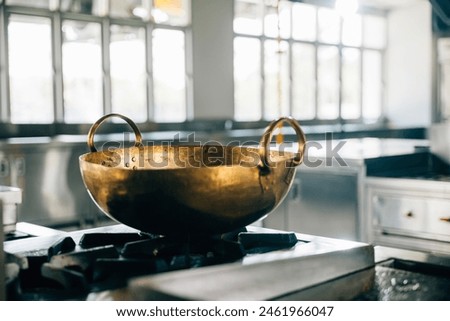 A professional kitchen in a modern restaurant features a shiny metal bowl atop the stove. Clean arrangement of chrome appliances equipment and new furniture. Bright gas service is working.