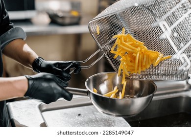 professional kitchen in restaurant of the hotel the chef takes out delicious french fries from the fryer - Shutterstock ID 2285149047