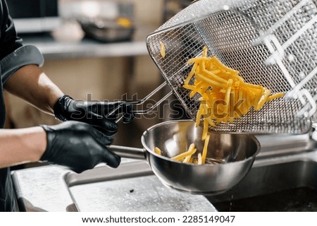 professional kitchen in restaurant of the hotel the chef takes out delicious french fries from the fryer