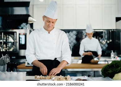 Professional kitchen: two chefs prepare food. The cook cuts mushrooms to prepare delicious dish.