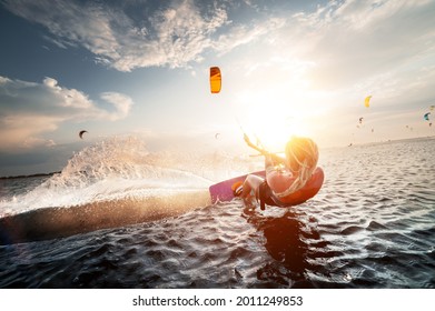Professional kite surfer woman rides on a board with a plank in her hands on a leman lake with sea water at sunset. Water splashes and sun glare. Water sports