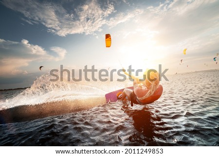 Professional kite surfer woman rides on a board with a plank in her hands on a leman lake with sea water at sunset. Water splashes and sun glare. Water sports