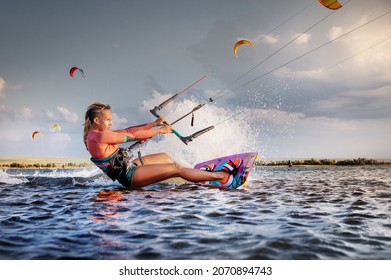 Professional kitesurfer young caucasian woman glides on a board along the sea surface at sunset against the backdrop of beautiful clouds and other kites. Active water sports