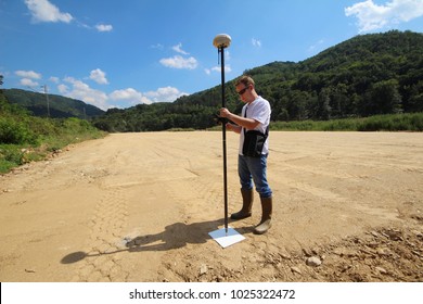 Professional land surveyor measures ground control point on a road construction site using GNSS rover on a pole