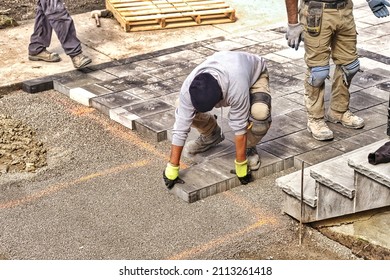 Professional landscape workers paving driveway interlock patio with stone brick at residential construction site. Contractor wearing safety protective cloth on  heavy installation yard work project.