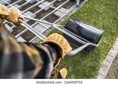 Professional Landscaper Compacting Natural Turfs Using Large Manual Grass Roller Next To Newly Building Patio Deck. Landscaping Industry Tools.