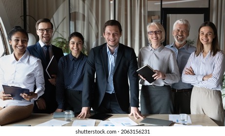 Professional Leader And Staff. Smiling Young Male Ceo Boss Executive Posing Ahead Of Successful International Work Group At Office Boardroom. Portrait Of Happy Diverse Business Partners Look At Camera