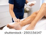 Professional leg waxing treatment at a beauty spa, with a beautician applying wax using a wooden spatula