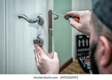 Professional locksmith worker installing the part of lock in wooden door by the screwdriver. Industrial theme