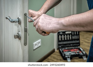 Professional locksmith worker installing, working with house door lock using screwdriver. Industrial theme
