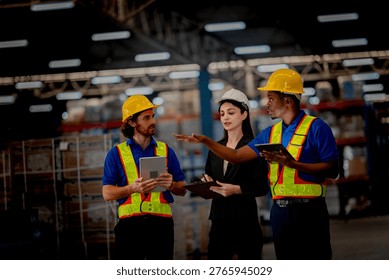 Professional logistics supervisor directing freight operations with diverse warehouse workers. Industrial staff wearing safety helmets planning safe cargo delivery.