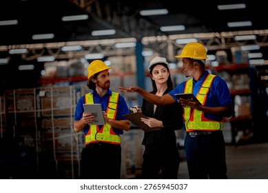 Professional logistics supervisor directing freight operations with diverse warehouse workers. Industrial staff wearing safety helmets planning safe cargo delivery.