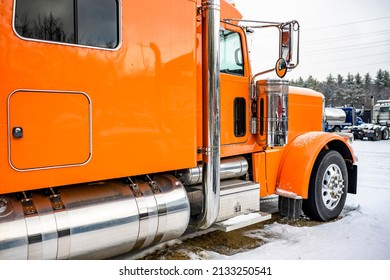 Professional Long Haul Classic Orange Big Rig Semi Truck Tractor With Extended Cab Standing Without Semi Trailer For Truck Driver Rest On The Winter Truck Stop Parking Lot Covered With Snow And Ice