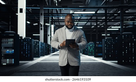 IT professional looking over data center checkup checklist paperwork on tablet. African american man walking in server farm, reading documentation files on device, camera A