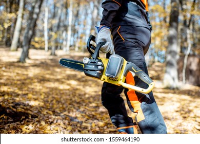 Professional lumberjack in protective workwear walking with a chainsaw in the forest, close-up on a saw