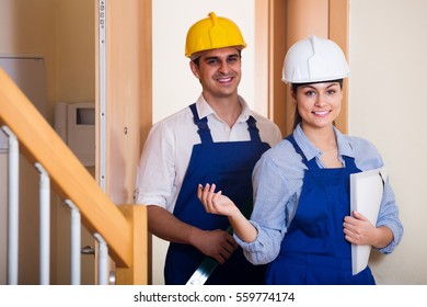 Professional Maintenance Crew Of Two Happy Spanish Specialists In Helmets Indoors