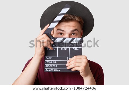 Professional male actor ready for shooting film, holds movie clapper, prepares for new scene, wears special clothes, isolated on white background. Handsome young man poses with clapboard in studio