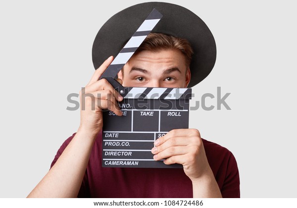 Professional male actor ready for shooting film,\
holds movie clapper, prepares for new scene, wears special clothes,\
isolated on white background. Handsome young man poses with\
clapboard in\
studio