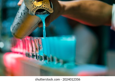 Professional Male Bartender Pouring Mixed Blue Liquor Cocktail Drink From Cocktail Shaker Into Shot Glass On Bar Counter At Nightclub. Mixologist Barman Making Alcoholic Drink Serving To Customer