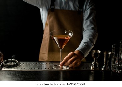 Professional Male Bartender Serving Delicious Golden Brown Cocktail On The Martini Glass On The Bar Counter