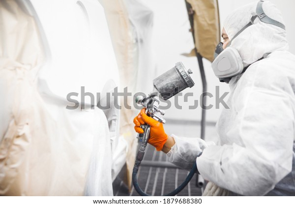 Professional male car painter is\
painting in garage by airbrush. Worker paints vehicle with spray\
gun.
