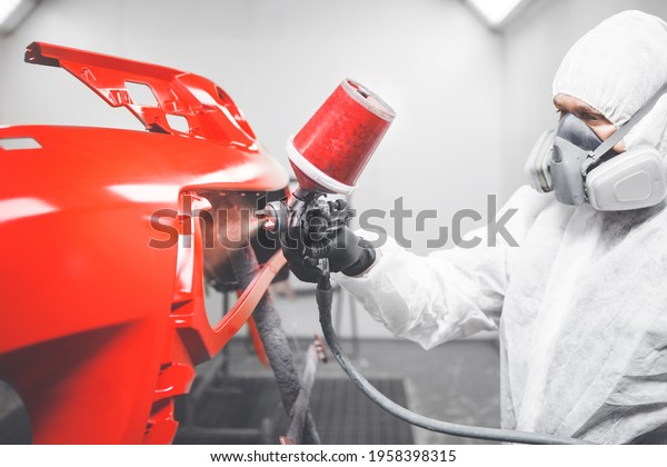 Professional male car painter is painting in\
garage by airbrush. Man works with spray\
gun.