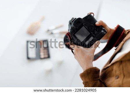Professional male content photographer working in photostudio, shooting cosmetics, focus on modern photocamera with blank display, above view