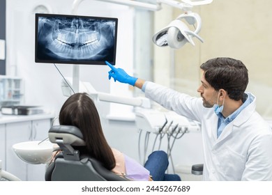 Professional male dentist showing x-ray footage of teeth to female patient in clinic office - Powered by Shutterstock