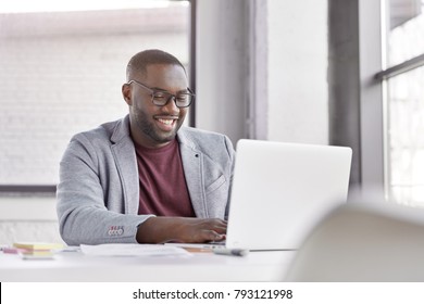 Professional male economist searches needed information on portable computer, happy to recieve high net profit, spends important banking operation. Black male trader analyzes financial market - Shutterstock ID 793121998