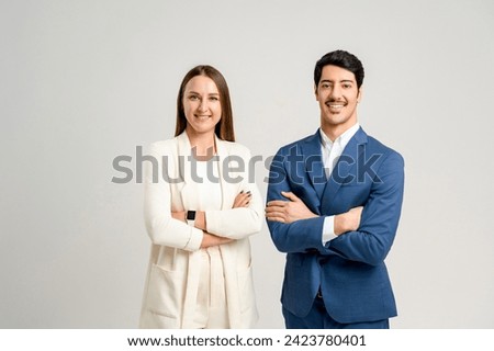 A professional male and female team, in sharp business attire, standing side by side with arms crossed. This image showcases the cooperative spirit and strategic planning