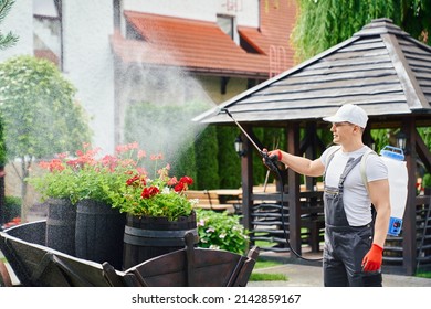 Professional male gardener in uniform, safety glasses and gloves using aerosol chemical protection from pests while working at garden. Concept of people, plants and seasonal work. 