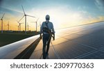 Professional Male Green Energy Engineer Walking On Solar Panel, Wearing Safety Belt And Hard Hat. Man Inspecting Sustainable Energy Farm With Wind Turbines. VFX Edit Visualizing Flow of Electricity.